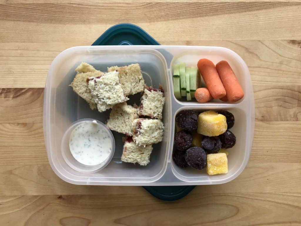 Homemade lunchable with peanut butter and jelly, carrots, cucumbers, mango, and cherries