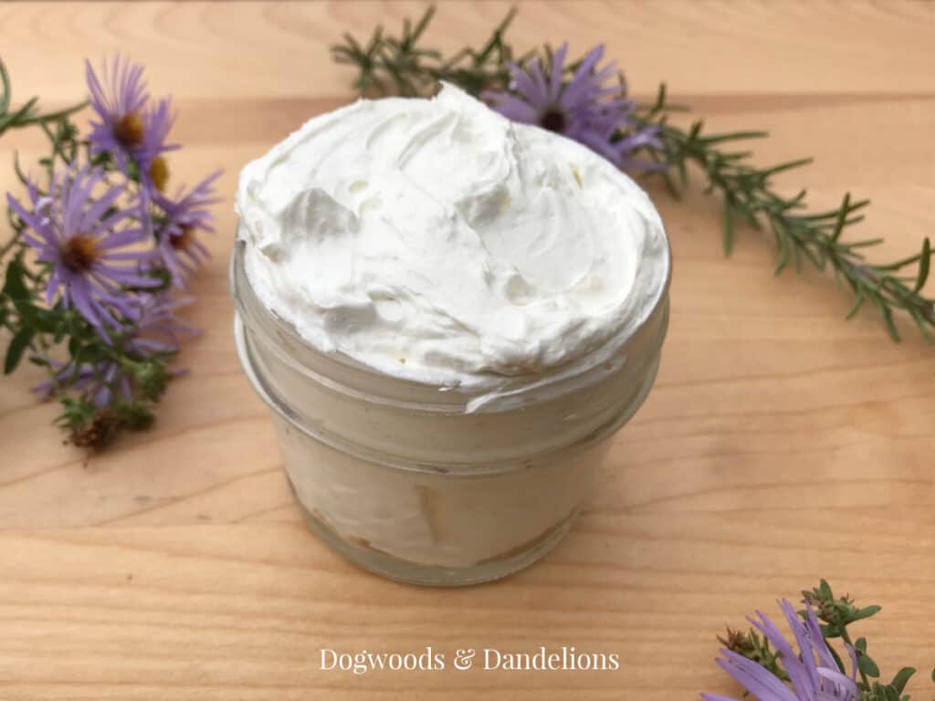 a jar of homemade body butter surrounded by rosemary and asters