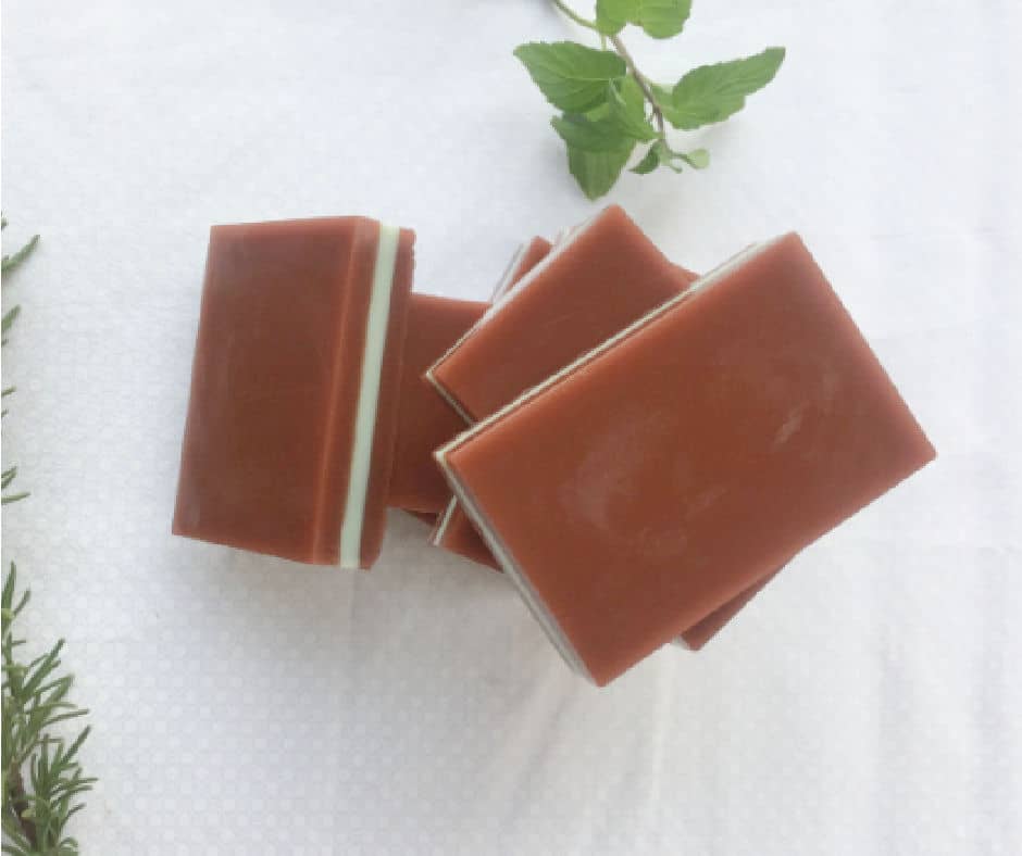 bars of chocolate mint soap stacked together and surrounded by basil and rosemary