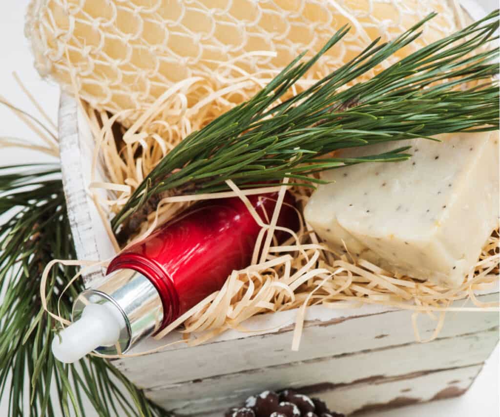 gift basket with pine needles, cloth, bar of soap, and bottle of serum