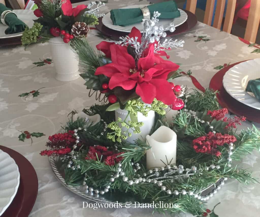a table set for Christmas with candles, poinsettias, greenery, and beads