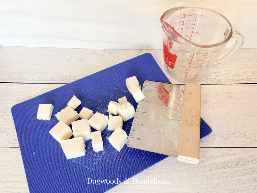 goat milk soap cubes on a blue cutting mat with a pyrex container and a bench scraper.