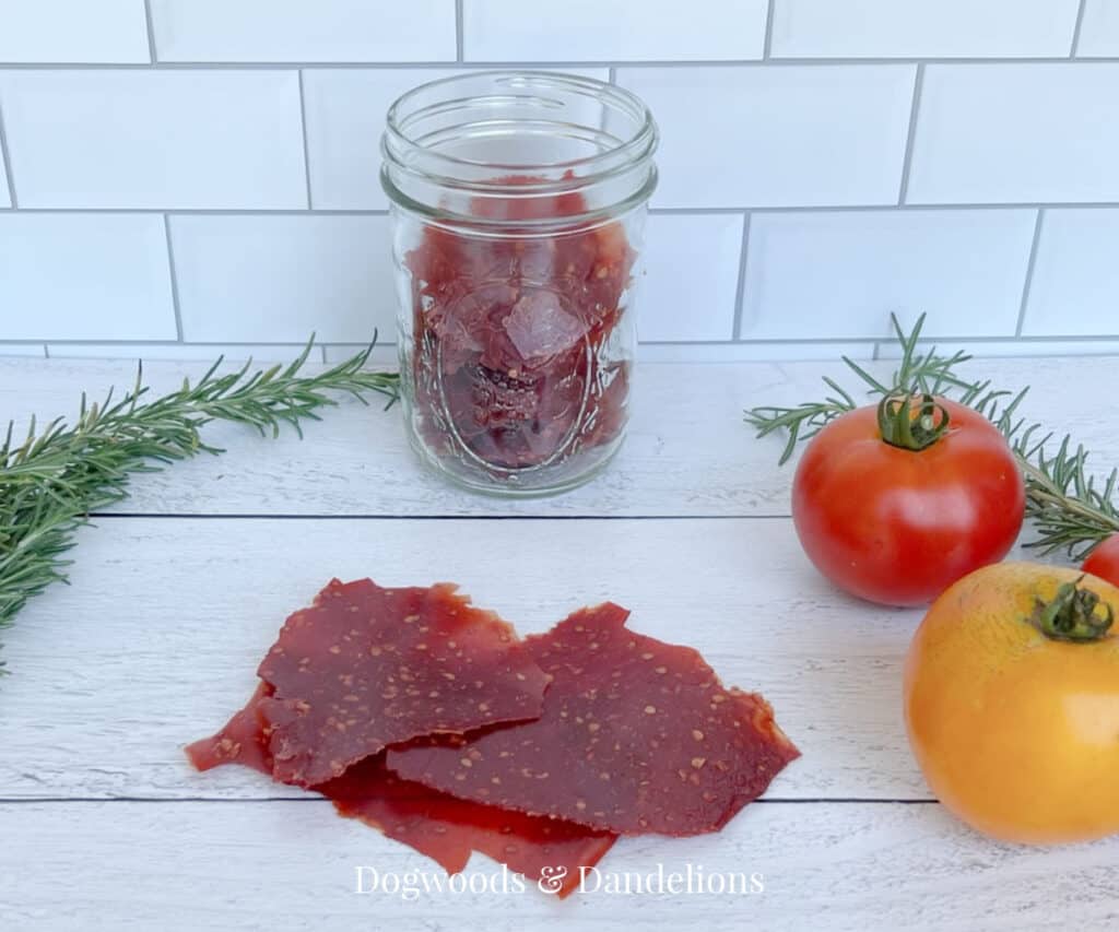 a jar of dehydrated tomato sauce with sheets of dried sauce and tomatoes and rosemary