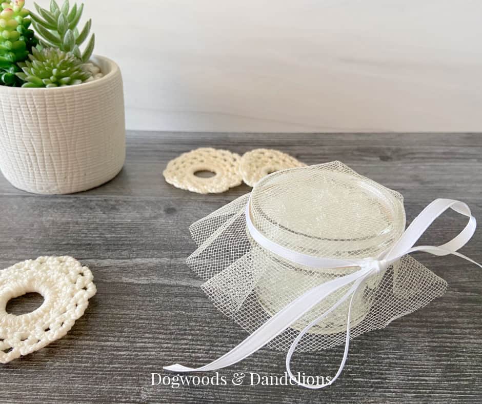 a gel air freshener covered with tulle, tied with a white bow, and surrounded by crocheted snowflakes and a succulent