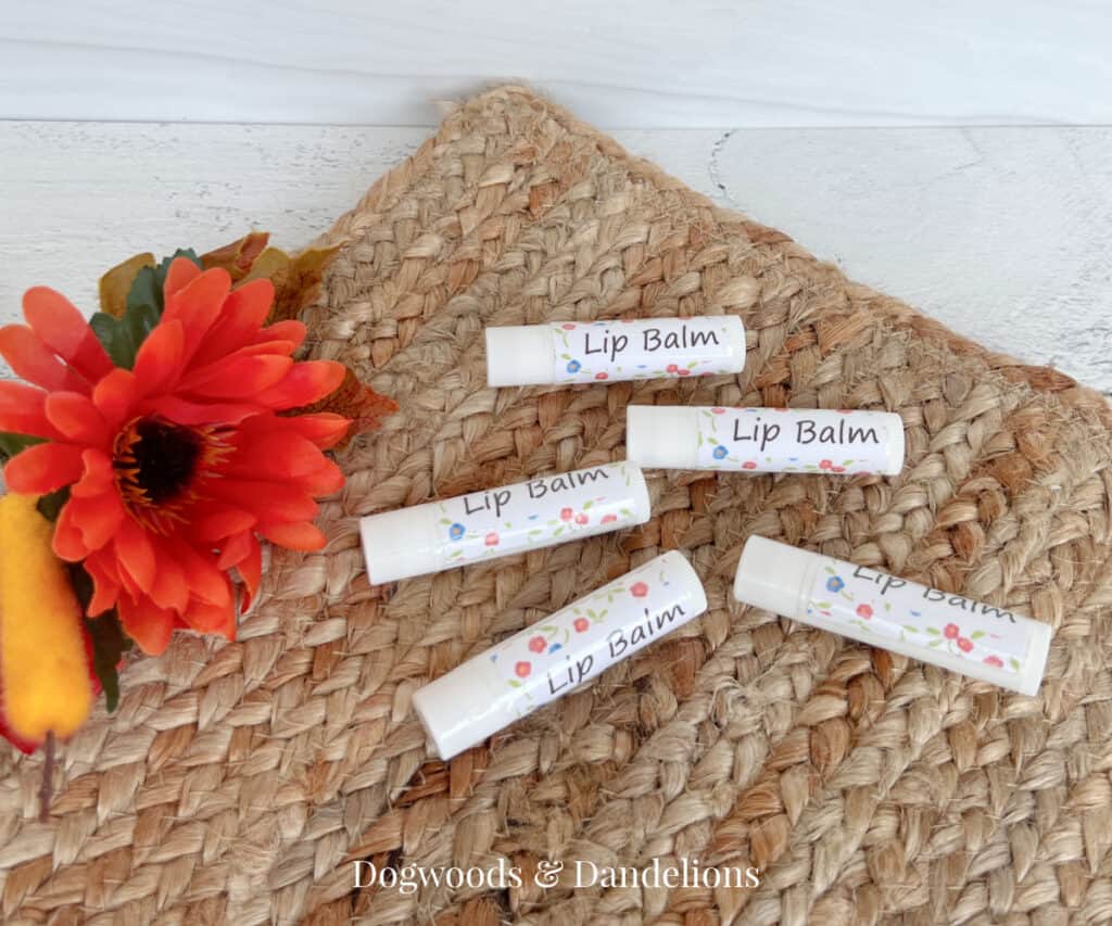 5 tubes of lip balm on a brown woven mat beside an orange flower and leaves.