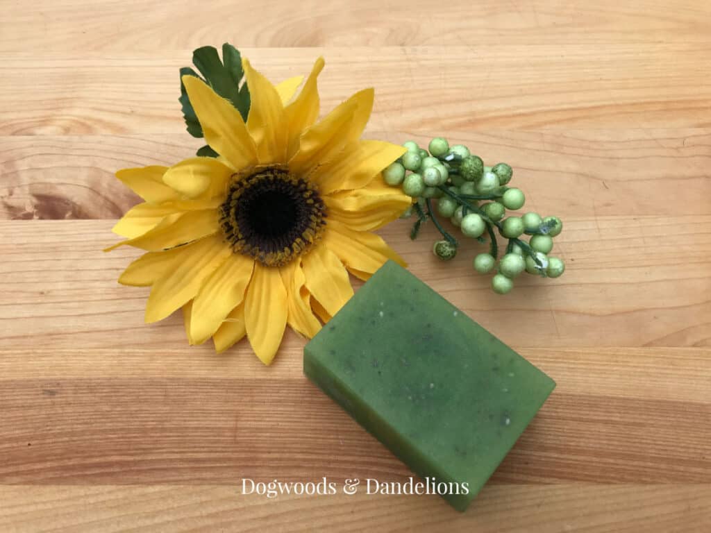 a green rectangle soap beside a yellow flower and greenery.