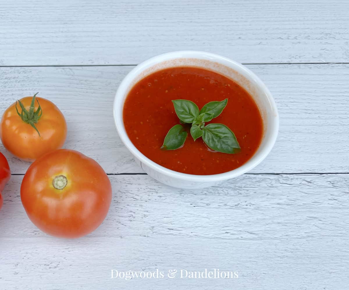 a bowl of tomato sauce with basil and tomatoes on the side