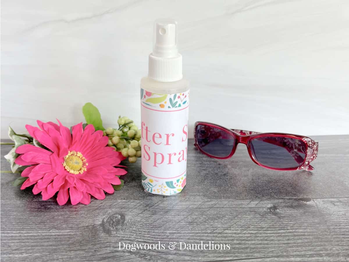 a bottle of after sun spray beside a flower, greenery, and a pair of sunglasses
