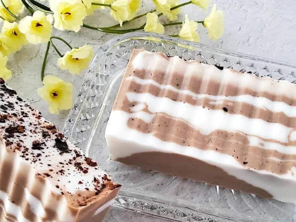 2 bars of chocolate vanilla soap beside yellow flowers.