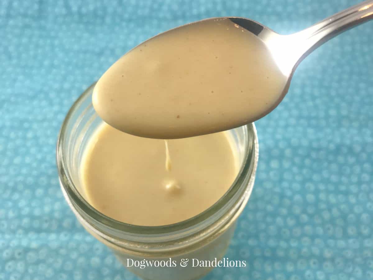 honey mustard dressing and dip in a jar with a spoon above it dripping dressing