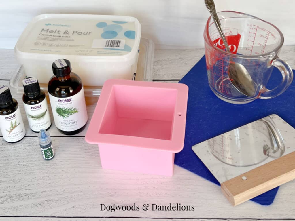 soap making supplies including soap base, a mold, essential oils, cutting mat, pyrex container, spoon, bench scrape.